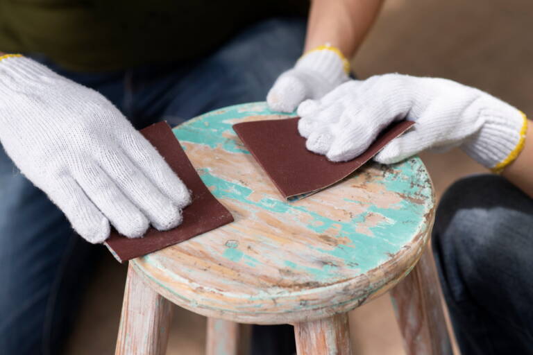 Carteggiatura manuale di uno sgabello in legno con abrasivi per legno