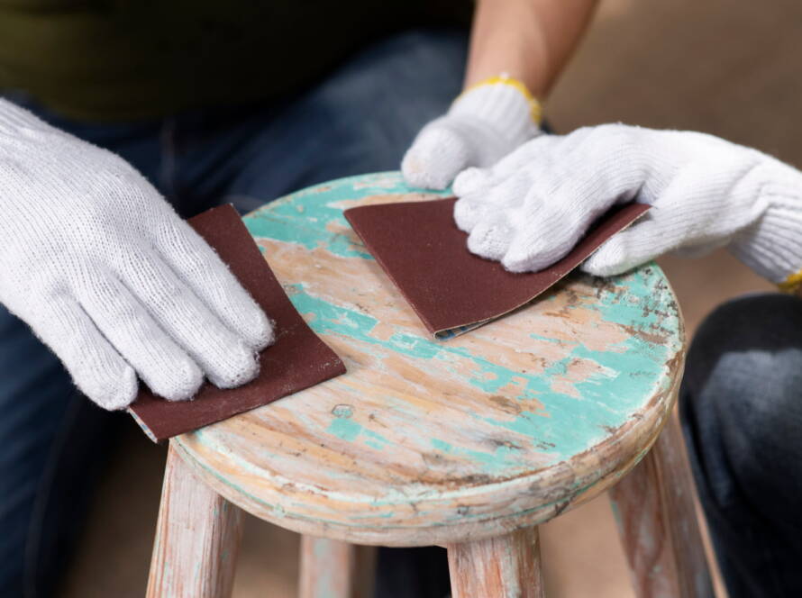 Carteggiatura manuale di uno sgabello in legno con abrasivi per legno