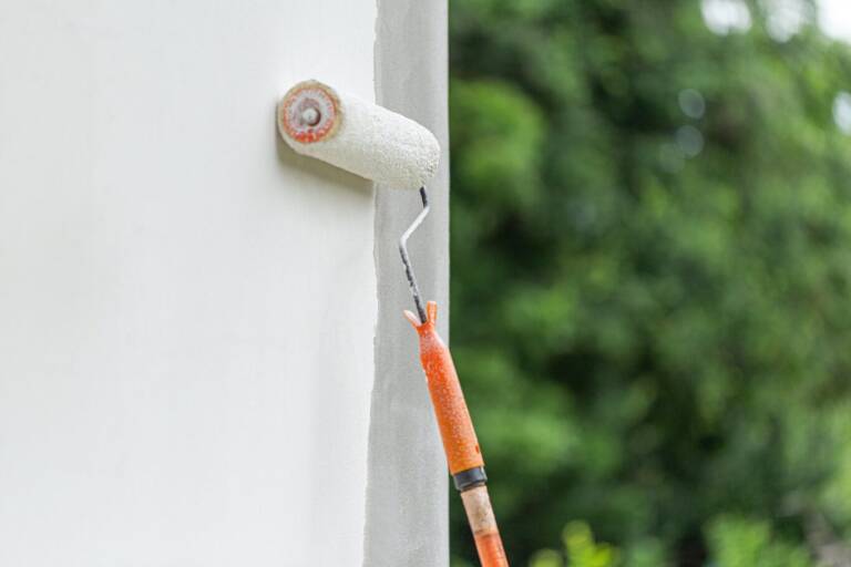Rullo che applica pittura murale bianca su una parete esterna durante la ristrutturazione
